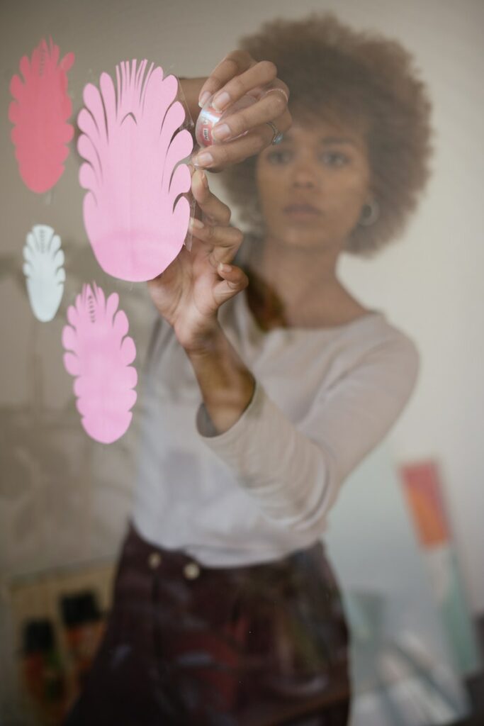 Concentrated black female artisan sticking paper flowers on glass wall