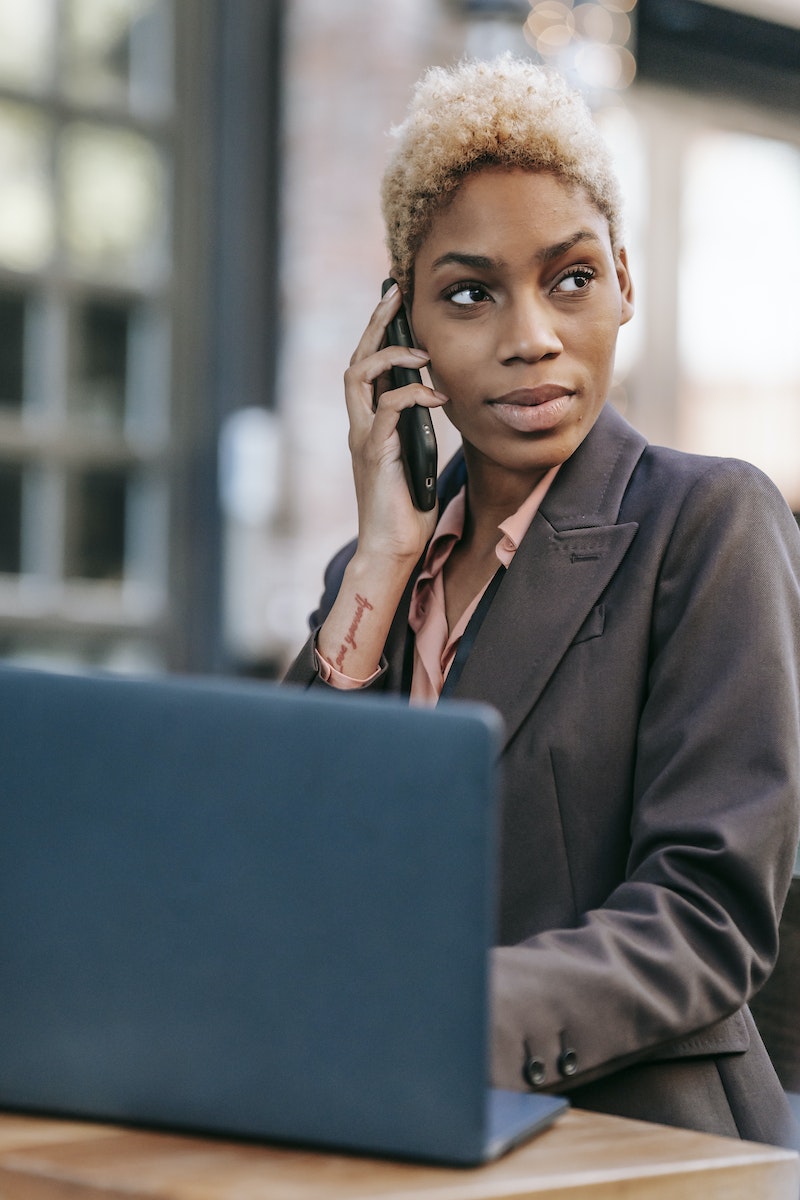 Black woman talking on smartphone and browsing laptop for work